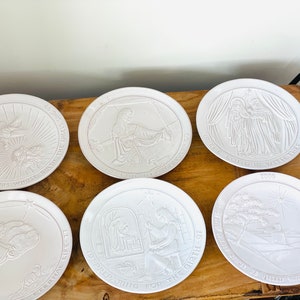 May include: Six white ceramic plates with raised images and text. The plates depict scenes from the Nativity story. The text on the plates includes verses from the Bible.