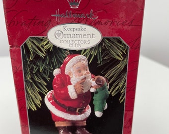 May include: A Hallmark Keepsake Ornament from the Collector's Club, featuring Santa Claus in a red suit with a white beard, holding a puppy in a green stocking. The box is red with the text "New Christmas Friend".