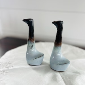 May include: Two ceramic bud vases with a tall, slender neck and a wide, rounded base. The glaze features a gradient transition from a glossy black at the top, through a band of warm brown, down to a pale, light blue finish at the bottom.