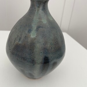 May include: A small, dark gray ceramic vase with a speckled glaze. The vase has a rounded body and a narrow neck.