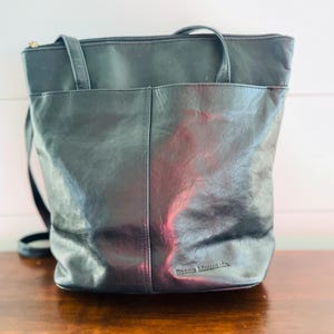 May include: Black leather tote bag with a shoulder strap and two handles. The bag has a front pocket and a zipper closure. The brand name "Stone Mountain" is visible on the bottom of the bag.