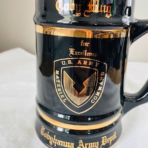 May include: Black ceramic Toby Mug with gold trim. The mug features the U.S. Army Materiel Command logo and the text "Toby Mug for Excellence" and "Tobyhanna Army Depot".