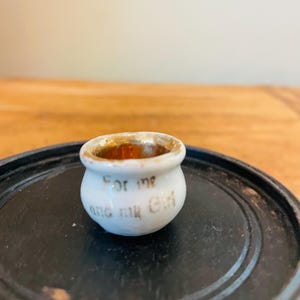 May include: A small white ceramic pot with gold trim and the words "For me and my Girl" written on the side.
