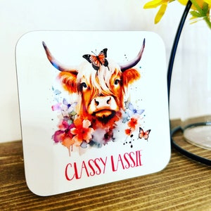 A Gorgeous Scottish Highland Cow Print Drinks Coaster with a Sweet Highland Cow Adorned With Flowers & Butterflies & Text Reading Classy Lassie Underneath