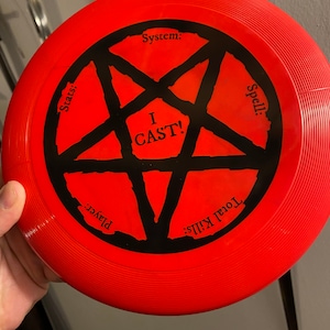 May include: A red frisbee with a black pentagram and the words "I CAST!" in the center. The frisbee also has the words "System:", "Stats:", "Spell:", "Player:", and "Total Kills:" around the pentagram.