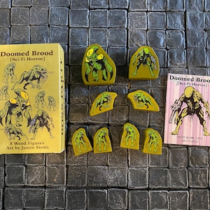 May include: A set of eight green and yellow painted wooden figures depicting a sci-fi horror creature. The figures are packaged in a box with the text "Doomed Brood [Sci-Fi Horror] 8 Wood Figures Art by Justin Sirois".