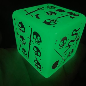 May include: A green glow-in-the-dark cube with black skull and sword designs. The cube is a decorative object.