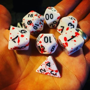 Może przedstawiać: Zestaw sześciu białych kości do gry z czerwonymi plamami i czarnymi liczbami. Kości są ponumerowane od 1 do 12.