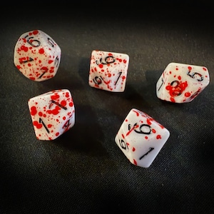 May include: Five white dice with black numbers and red splatter paint. The dice are on a black surface.