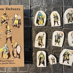 Puede incluir: Un conjunto de figuras de madera "Shadow Delvers". El conjunto incluye una caja con ilustraciones de varios personajes de fantasía y diez figuras de madera individuales con diseños de personajes únicos. Las figuras están sobre una superficie texturizada.