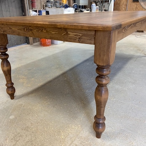 Peut inclure: Une table &agrave; manger rectangulaire en bois avec une finition teint&eacute;e brun moyen et un grain de bois visible. La table pr&eacute;sente une surface sup&eacute;rieure plate avec un bord droit et quatre pieds tourn&eacute;s avec un profil arrondi et d&eacute;coratif.