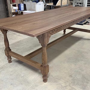 May include: A large, rectangular, wooden table with a brown stain. The table has a simple, rustic design with turned legs and a single stretcher.