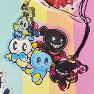May include: A collection of clear acrylic charms featuring cartoon characters in various colors. The charms include a white angel character with a blue halo, a black character with a sinister grin, and other colorful creatures.
