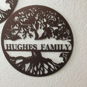 May include: A brown metal tree of life wall decor with the text "HUGHES FAMILY" in a banner below the tree.