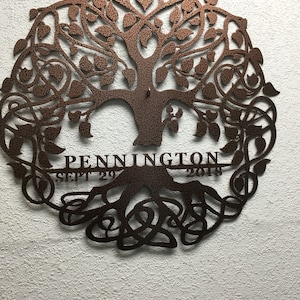 May include: A brown metal tree of life wall art with intricate details. The tree has a thick trunk and branches with leaves. The roots are intertwined and spread out at the bottom. The words "PENNINGTON" and "SEPT 29 2018" are inscribed on the tree.