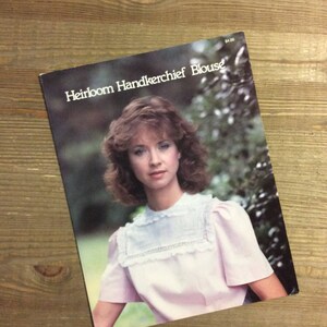 May include: A vintage sewing pattern booklet featuring a woman wearing a pink and white heirloom handkerchief blouse. The cover of the booklet reads "Heirloom Handkerchief Blouse".