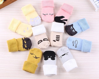 May include: A collection of ten baby socks in various colors including yellow, pink, blue, beige, and gray. Each sock features a unique graphic design such as cat faces, fish, birds, or simple patterns, with folded cuffs and soft, knit fabric construction.