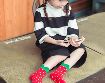 May include: A young person wearing a black and white striped top and black shorts, paired with red socks featuring a strawberry design. The socks have green cuffs and yellow seeds. The person is holding a smartphone.