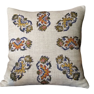 May include: A beige linen cushion with a floral pattern in shades of yellow, orange, blue, and green. The cushion is decorated with a repeating pattern of stylised flowers.