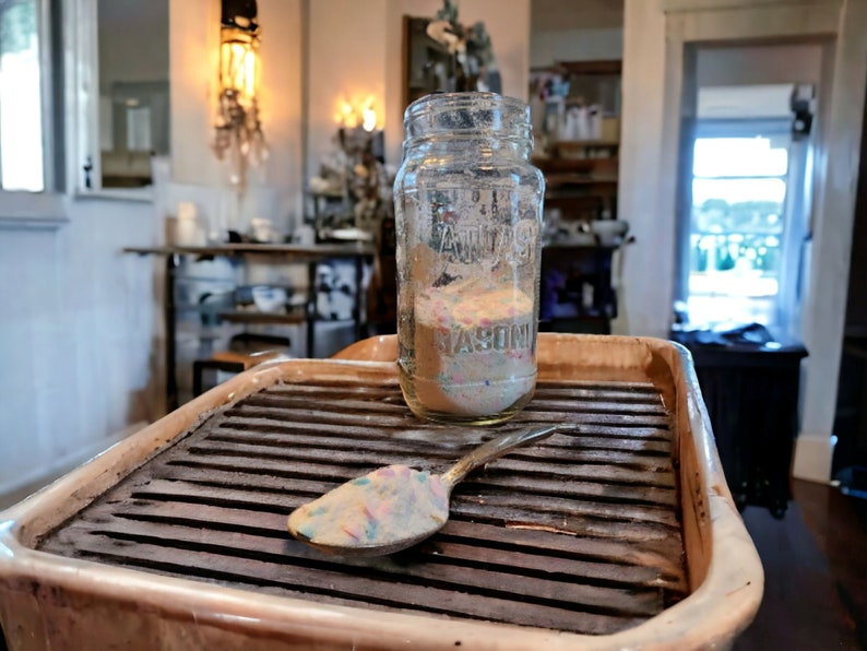 May include: A clear glass jar with a lid, filled with colorful sprinkles, sits on a brown tray with a metal spoon. The jar has the word "MASON" printed on the bottom.
