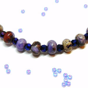 Pu&ograve; includere: Un braccialetto di perline viola e marroni con perline di vetro blu scuro. Il braccialetto &egrave; su uno sfondo bianco con perline blu iridescenti sparse.