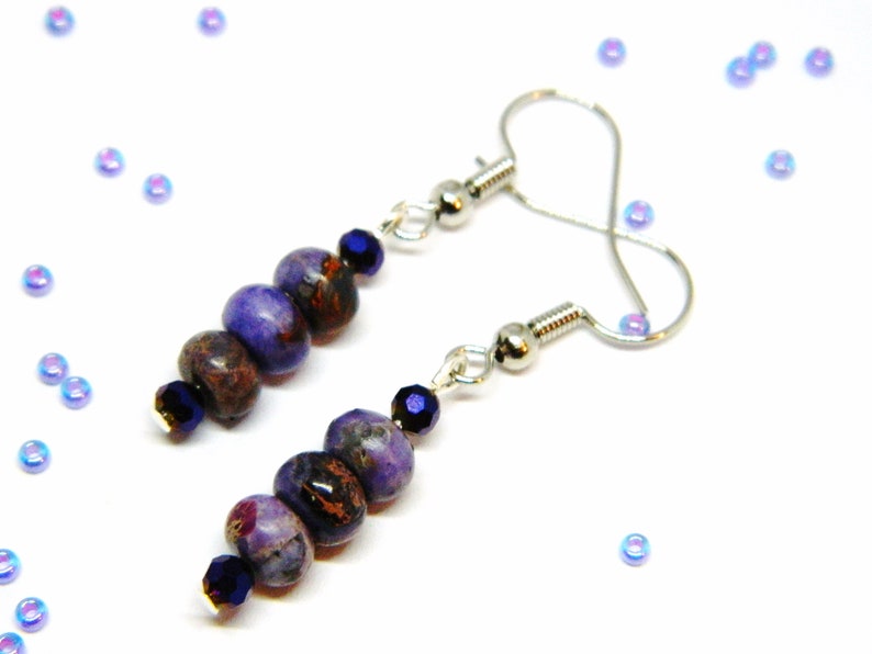 Pu&ograve; includere: Orecchini con perline di pietre preziose viola e marroni con ganci d'argento. Le perline sono rotonde e hanno un aspetto screziato.