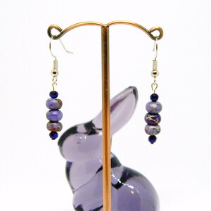 Pu&ograve; includere: Orecchini pendenti in pietre preziose viola e blu con ganci d'argento. Gli orecchini presentano un gruppo di perle rotonde.