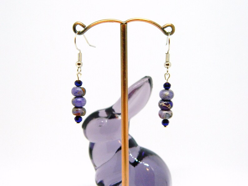 Pu&ograve; includere: Orecchini pendenti in pietre preziose viola e blu con ganci d'argento. Gli orecchini presentano un gruppo di perle rotonde.