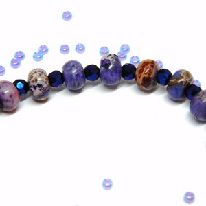 Pu&ograve; includere: Primo piano di un braccialetto di pietre preziose viola e blu con perline distanziatrici blu scuro. Il braccialetto &egrave; realizzato con perline rotonde e sfaccettate.