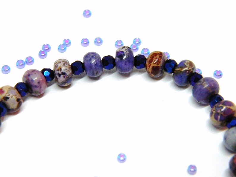 Pu&ograve; includere: Primo piano di un braccialetto di pietre preziose viola e blu con perline distanziatrici blu scuro. Il braccialetto &egrave; realizzato con perline rotonde e sfaccettate.