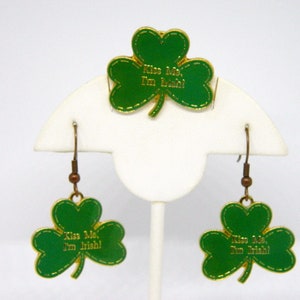May include: A set of gold-tone earrings and a pin featuring green shamrock charms with the text "Kiss Me, I'm Irish!"
