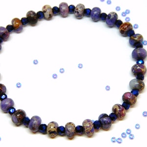 Pu&ograve; includere: Un braccialetto di pietre preziose viola e marroni con perline di vetro blu scuro. Il braccialetto &egrave; su uno sfondo bianco.
