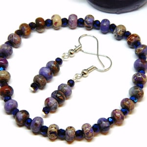 Pu&ograve; includere: Una collana di perline viola e marroni con orecchini abbinati. La collana e gli orecchini sono realizzati con piccole perline rotonde e metallo argentato.