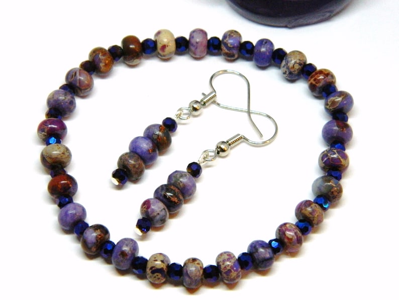 Pu&ograve; includere: Una collana di perline viola e marroni con orecchini abbinati. La collana e gli orecchini sono realizzati con piccole perline rotonde e metallo argentato.