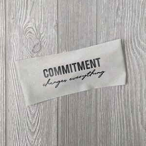 Op de afbeelding: Een grijze stoffen banner met de tekst "COMMITMENT changes everything" in het zwart gedrukt.