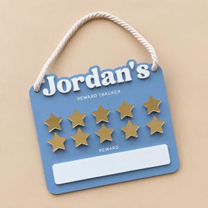 May include: A blue reward tracker sign with a white rope hanger. The sign features the white text Jordan's, the words REWARD TRACKER, ten gold star icons arranged in two rows, and a white rectangular space labeled with the word REWARD.