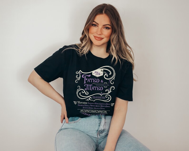 A woman wearing a black shirt that says The Fated and Mated Maasverse Tour.This is accompanied with white swirls and whirls, and other embellishments. Then it has a featuring section underneath with names from SJM books.