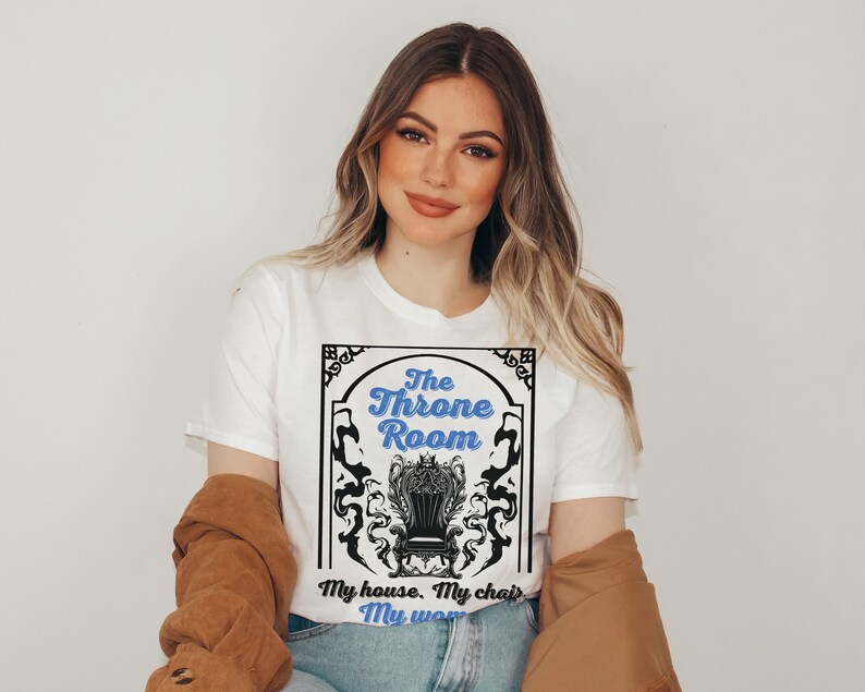 A woman wearing a white colored T-shirt featuring  text that reads "The Throne Room, My House. My Chair. My Woman" accompanied by an intricate image of a throne surrounded by mysterious shadow tendrils.