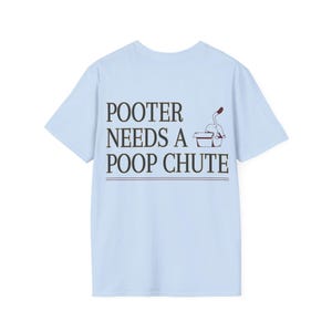 May include: Light blue t-shirt with the text "POOTER NEEDS A POOP CHUTE" in dark brown. A small illustration of a toilet with a plunger is to the right of the text. The shirt is a casual wear item.