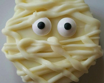 May include: A white chocolate-covered cookie decorated to look like a mummy. The cookie has two white candy eyes with black pupils.