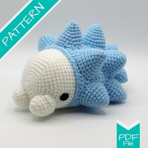 Puede incluir: Juguete de peluche tejido a ganchillo en azul claro y blanco. El juguete tiene un cuerpo redondeado con protuberancias puntiagudas a lo largo de la espalda. La cara es blanca con un ojo negro. La imagen incluye la palabra "PATTERN" y "PDF File".