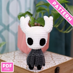 May include: A handmade crochet figure of a character with a white head, large black eyes, and a gray cloak. The figure is labeled "1Up Crochet" and "PDF File". A pink banner reads "PATTERN".