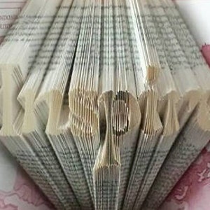 May include: A book art sculpture of the word "Inspire" created by folding the pages of a book. The sculpture is made from a book with a white cover and the pages are folded to create the letters.