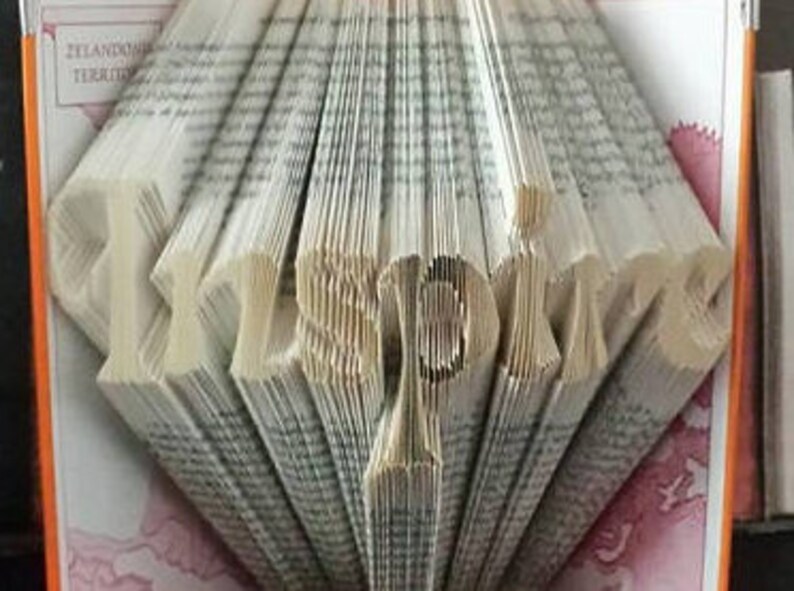 May include: A book art sculpture of the word "Inspire" created by folding the pages of a book. The sculpture is made from a book with a white cover and the pages are folded to create the letters.