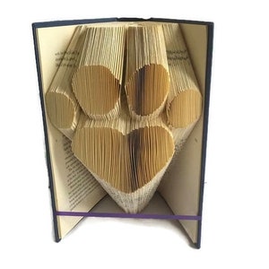 May include: A book art sculpture of a paw print made from folded pages. The book is bound in a dark blue cover and has a purple ribbon tied around it.
