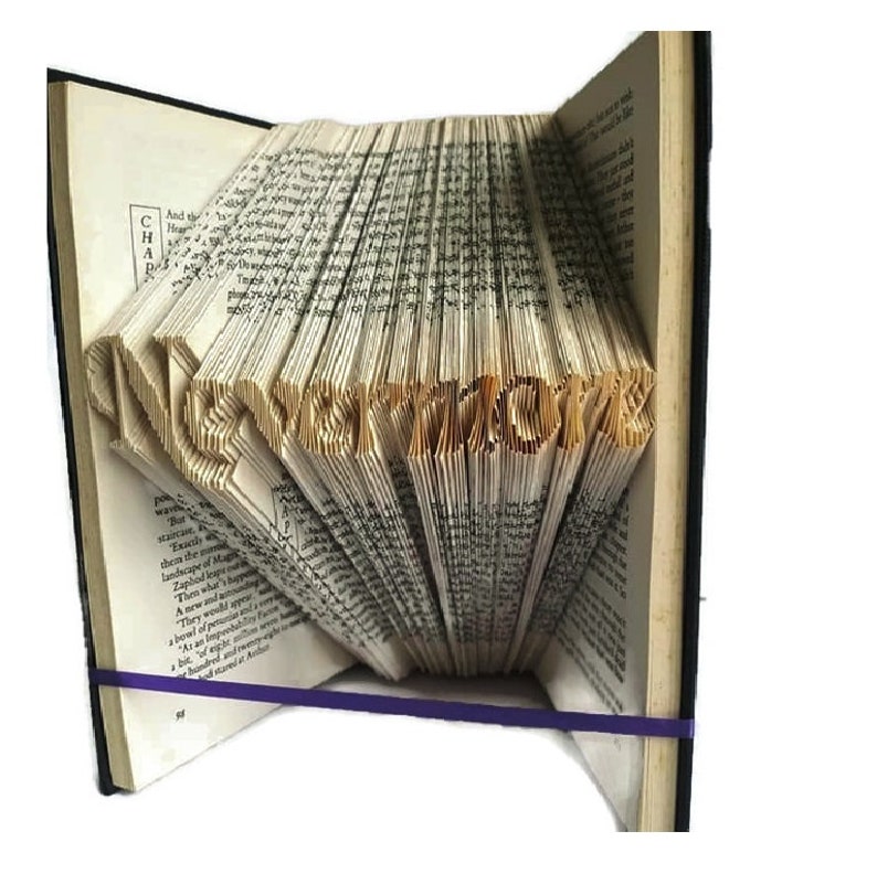 May include: A book art sculpture with the word "NEVERMORE" folded into the pages. The book is open and the pages are folded to create the word. The book is bound in brown leather and has a purple ribbon tied around it.