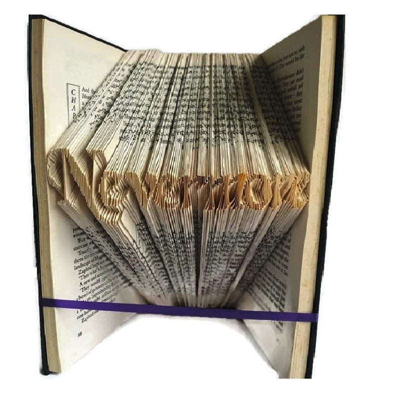 May include: A book with the word "remarkable" folded into the pages. The book is open and the pages are folded to create the word. The book is bound in brown leather and has a purple elastic band around it.