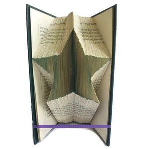 May include: A book with pages folded into a 3D star shape. The book is bound in a dark green cover and has a purple elastic band around it.