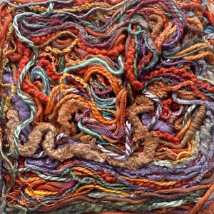 May include: Close-up of a textured textile art piece. The artwork features a dense arrangement of colorful yarns in shades of orange, red, purple, teal, and brown. The yarns are intertwined, creating a tactile and visually rich surface.