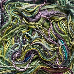 May include: Close-up of a tangled assortment of colorful yarn. The yarn features a variety of textures and shades, including greens, yellows, purples, and blues. Some strands are twisted, while others are smooth or textured, creating a visually rich display.